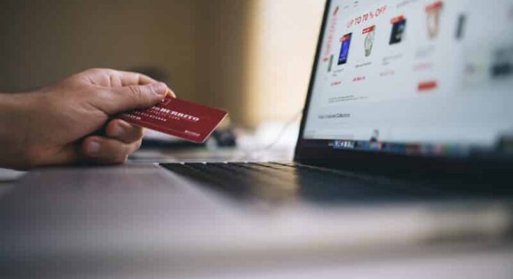 A person using technology to generate sales, holding a credit card in front of a laptop.