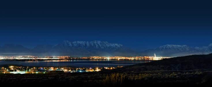 A panoramic night view of a brightly lit cityscape along a coastline, with silhouetted mountains in the background and clear skies above, making it one of the best places to start a tech company