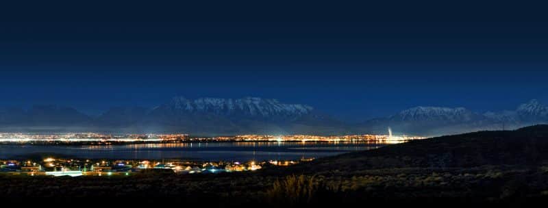 A panoramic night view of a brightly lit cityscape along a coastline, with silhouetted mountains in the background and clear skies above, making it one of the best places to start a tech company