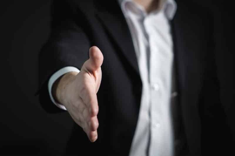 A businessperson in a dark suit extending a handshake, focusing on the hand with web tools that supercharge your job search in the blurred background.