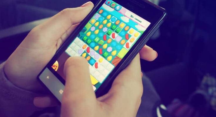 Close-up of a person's hands holding a smartphone, playing a colorful candy-themed mobile video game. The player is actively interacting with the game screen.