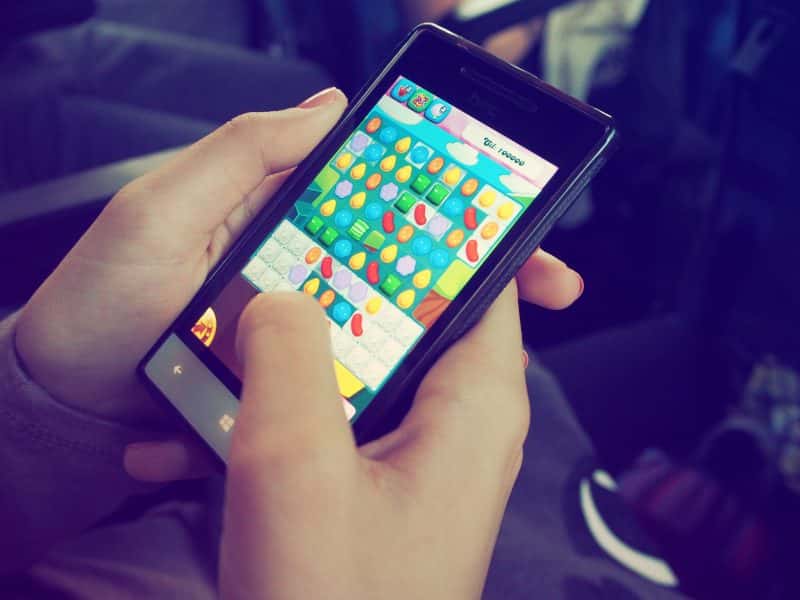 Close-up of a person's hands holding a smartphone, playing a colorful candy-themed mobile video game. The player is actively interacting with the game screen.