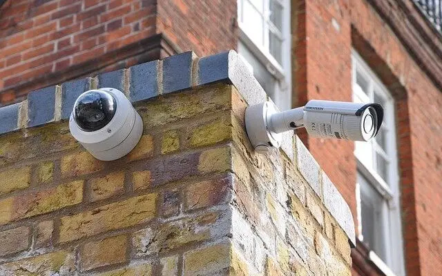 Two security cameras installed on the corner of an old brick building, one dome-shaped and the other cylindrical, monitoring the surroundings for alternative uses in security systems.