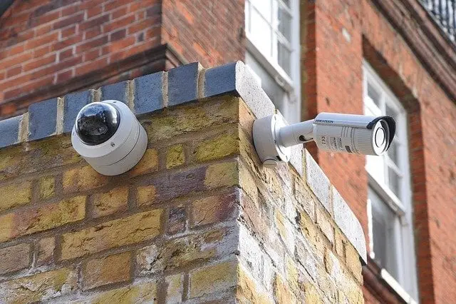 Two security cameras installed on the corner of an old brick building, one dome-shaped and the other cylindrical, monitoring the surroundings for alternative uses in security systems.