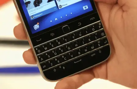 Hand holding a business phone with a physical qwerty keyboard, displaying social media applications on the screen.