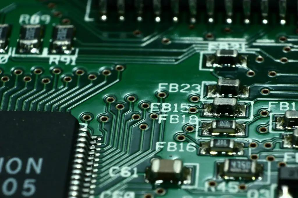 Close-up of a green PCB featuring various electronic components like resistors, microchips, and printed circuit pathways, highlighting the complexity of modern electronics.