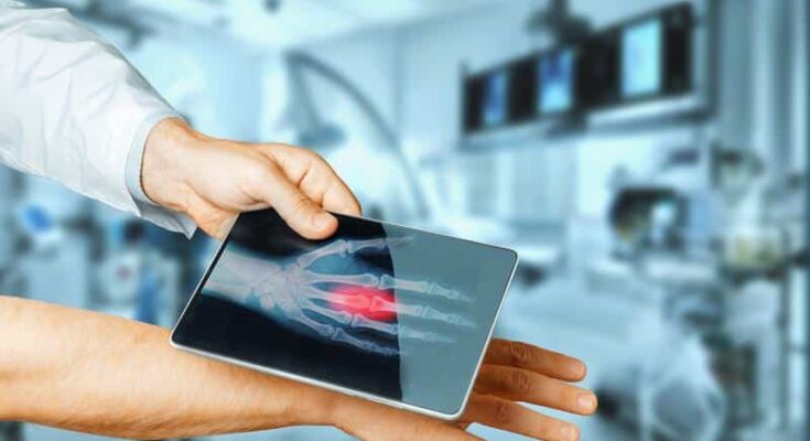 A healthcare professional holds a transparent digital tablet displaying a 3D image of a human heart, with advanced medical technology and a blurred hospital room in the background.