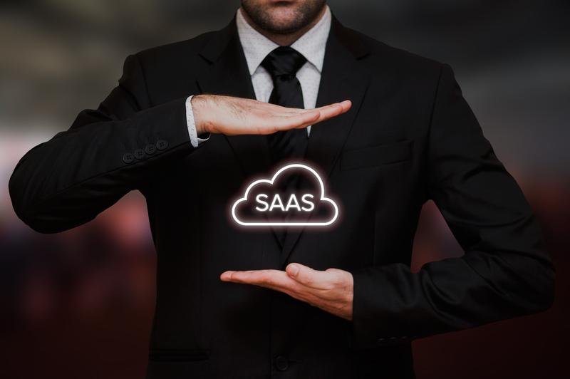 A man in a black suit gestures with his hands framing the glowing white text "Software as a Service" inside a cloud icon, symbolizing software as a service, against a blurred background.