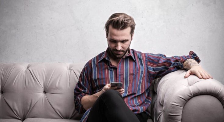 man sat on sofa reading phone