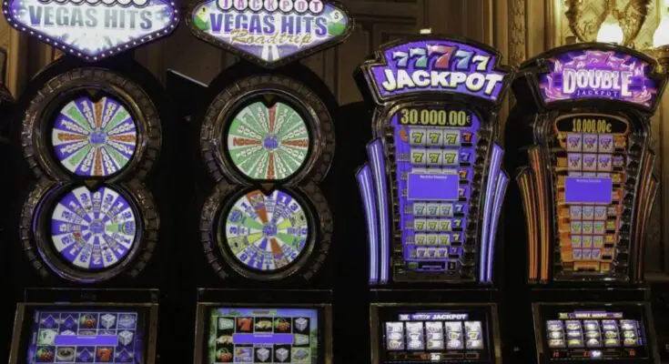 A row of colorful slot machines, including "vegas hits" and "jackpot," displays vibrant screens and illuminated signs in a lively casino setting.