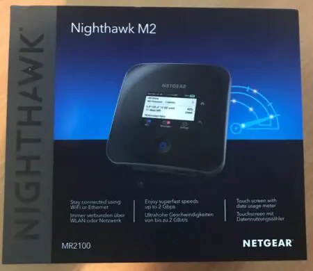 A Netgear Nighthawk M2 mobile router's packaging box displaying the device with a digital screen, and text highlighting features like 2 Gbps speeds and touchscreen interface.