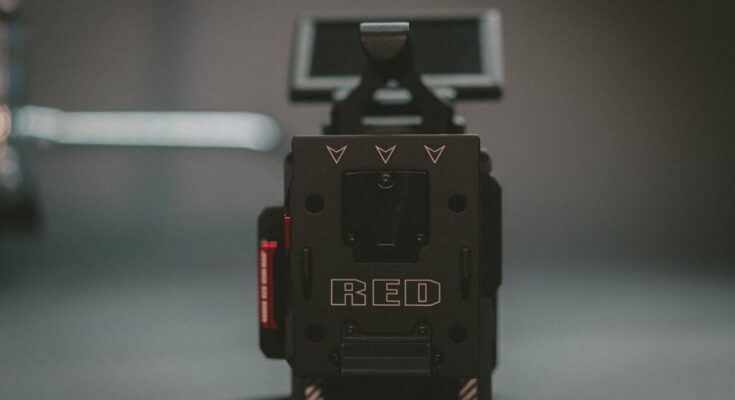 A close-up photo of a red digital cinema camera, focusing on the back of the camera body with the red logo prominently displayed. the background is blurred.