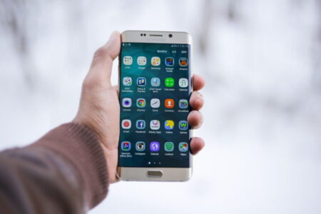 A hand holds a smartphone displaying various mobile online casino app icons with a blurry snow-covered background.
