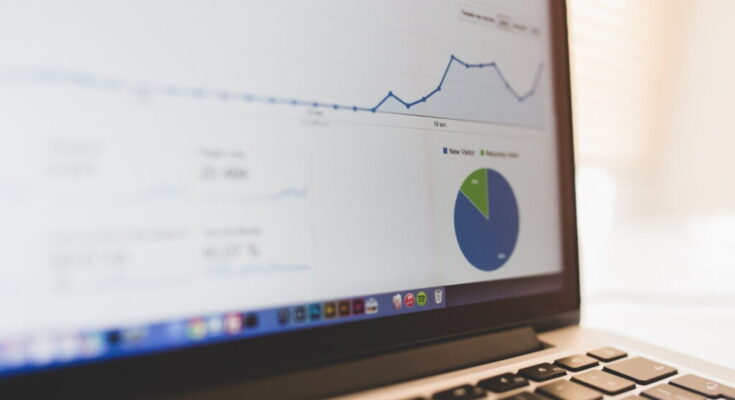 Laptop screen displaying a business graph with a rising line chart and a pie chart, indicating data analysis, placed on a desk with a blurred background.