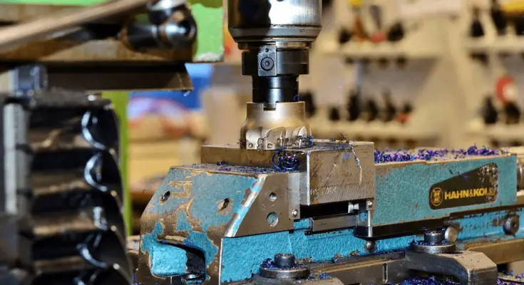 A close-up photo of a CNC milling machine in operation, with metal shavings visible around the drill and on the machine platform.