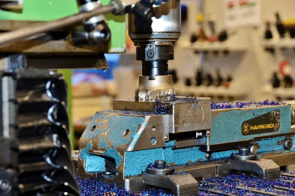 A close-up photo of a CNC milling machine in operation, with metal shavings visible around the drill and on the machine platform.
