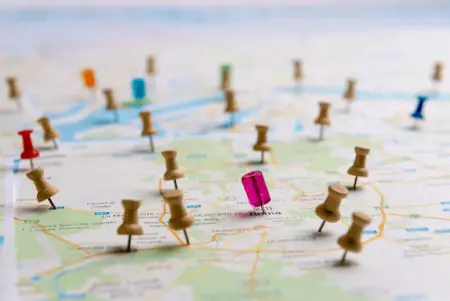 A close-up of a map covered with multiple colored pushpins, highlighting various geolocations, with a focus on a pink pin in the center.
