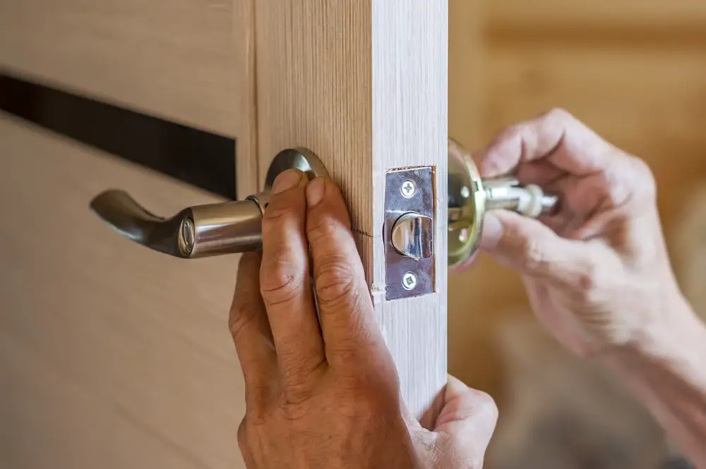 A person installs a modern metal door handle and lock on a wooden door, focusing on aligning the components correctly to enhance home security.