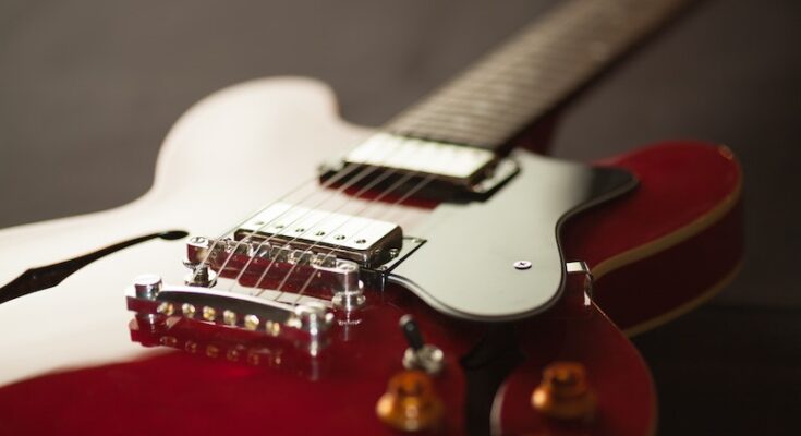 Close-up of a red and white electric guitar, focusing on its bridge and strings with a blurred background, highlighting the guitar's glossy finish and fine details.