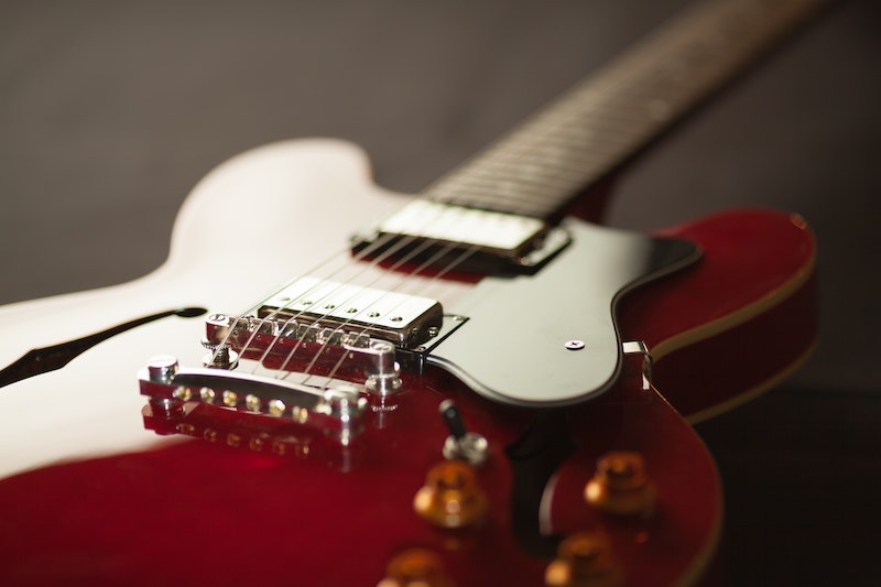 Close-up of a red and white electric guitar, focusing on its bridge and strings with a blurred background, highlighting the guitar's glossy finish and fine details.