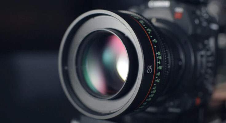 Close-up of a video camera lens focusing on 85mm, with reflections of light on the glass and visible aperture and distance scale markings.