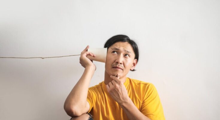 pensive ethnic man listening to answer in paper cup phone