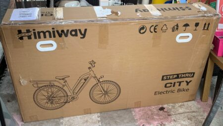 A large cardboard box labeled "Himiway" featuring a printed image of an electric bike with text "City Pedelec step thru electric bike." Safety and handling icons are visible at the top.