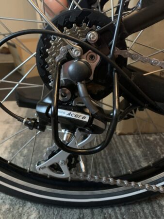 Close-up of a Himiway City Pedelec rear wheel showing details such as the derailleur, cogs, and spokes, with the derailleur branded "Shimano Acera.