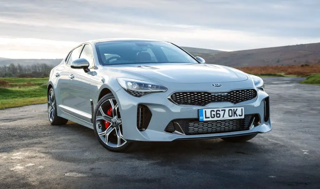 A silver Kia Stinger car parked on an open road with a scenic, hilly landscape in the background during the daytime.