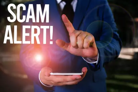 A man in a business suit holds a smartphone in one hand and points at the screen with the other, with the words "scam alert!" superimposed in bold text, emphasizing caution about affiliate