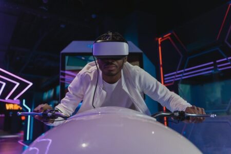 A young man wearing a VR headset intensely focuses while leaning over a futuristic gaming console in a neon-lit room, simulating deep game immersion in a virtual reality experience.