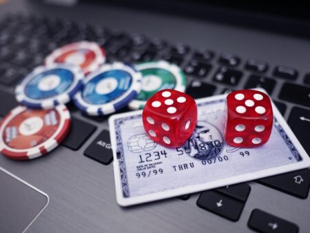 Two red dice on a credit card surrounded by casino chips on a laptop keyboard, symbolizing good online casino gambling.