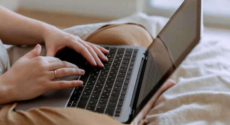 faceless woman using laptop while sitting on bed