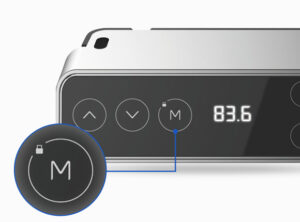 Close-up of a modern device, possibly part of a standing desk system, showing part of its digital display reading "83.6" and tactile buttons, highlighted with descriptions indicating a mode switch button.