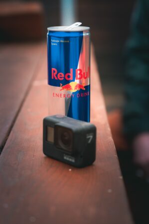 A co-branding collaboration between a Red Bull energy drink can and a GoPro camera on a wooden surface, with a blurred background emphasizing the items in focus.