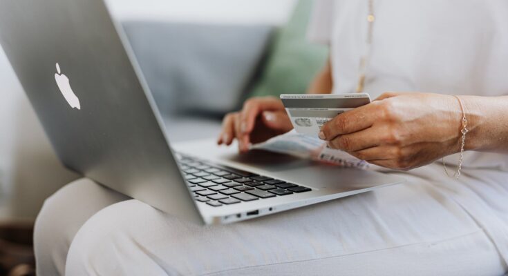 person using a macbook and holding a credit card