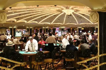 A vibrant casino floor with numerous guests engaged in games, including some of the best poker sites. Bright overhead lights illuminate the area, with gaming tables and slot machines visible. People are focused on their activities