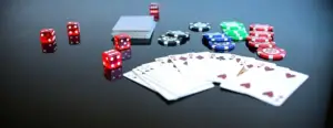 Various gambling items on a black surface, including red, white, and green poker chips from the best poker site, two packs of cards in a spread, and multiple red dice.