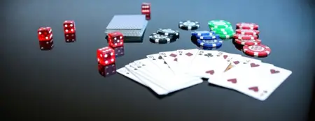 Various gambling items on a black surface, including red, white, and green poker chips from the best poker site, two packs of cards in a spread, and multiple red dice.