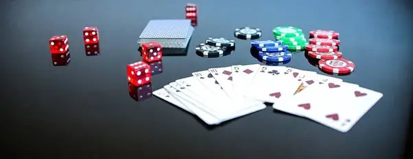Various gambling items on a black surface, including red, white, and green poker chips from the best poker site, two packs of cards in a spread, and multiple red dice.