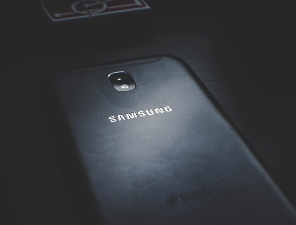 A close-up of a Samsung smartphone in a dark setting, optimized for gaming, with emphasis on its rear camera and brand logo illuminated by soft light.
