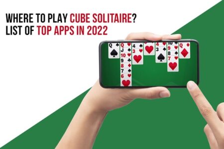 Hands holding a smartphone displaying a game of solitaire cubes, with text above reading "where to play solitaire cubes? list of top apps in 2022.