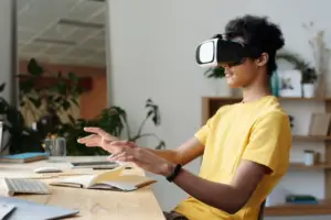 A person wearing a VR headset sits at a desk, interacting with an unseen virtual environment, surrounded by a laptop, books, and a technology trends office setting.