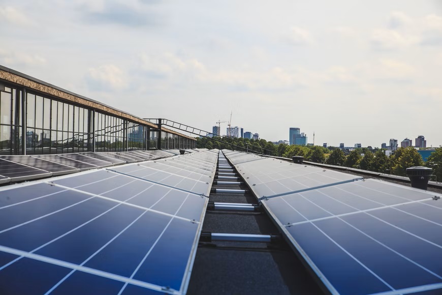 Solar panels, representing growing industries, are installed on a rooftop, extending toward the horizon with a city skyline in the background under a cloudy sky.