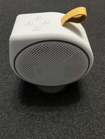 A portable white BenQ GV30 projector with a yellow carrying strap, control buttons on top, placed on a textured dark surface.