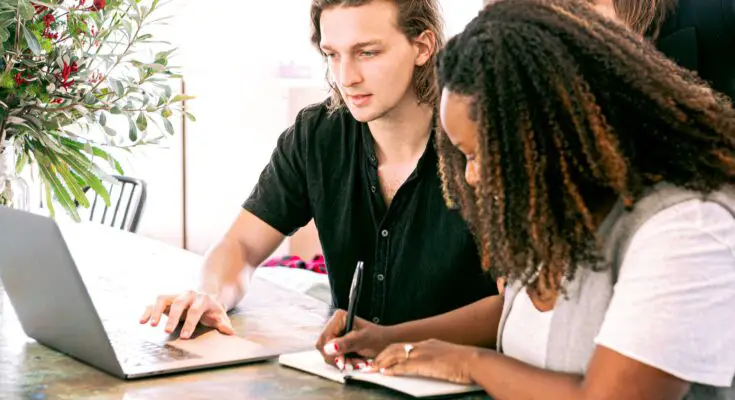 man working on laptop while woman takes notes