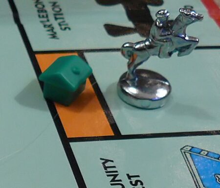 A close-up view of a video gaming-inspired monopoly game board showing a silver knight chess piece token and a green house on properties.