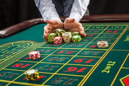 A person in a business suit at a roulette table arranging colorful casino chips on various betting numbers, captured from a close, slightly overhead angle in the betting industry.