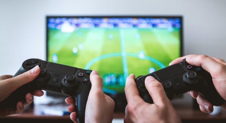 two people holding black gaming consoles