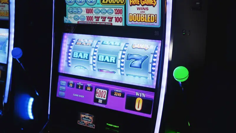 Close-up of a jackpot slot machine screen displaying a near win with two sevens and a bar, surrounded by colorful lights, with credits showing.